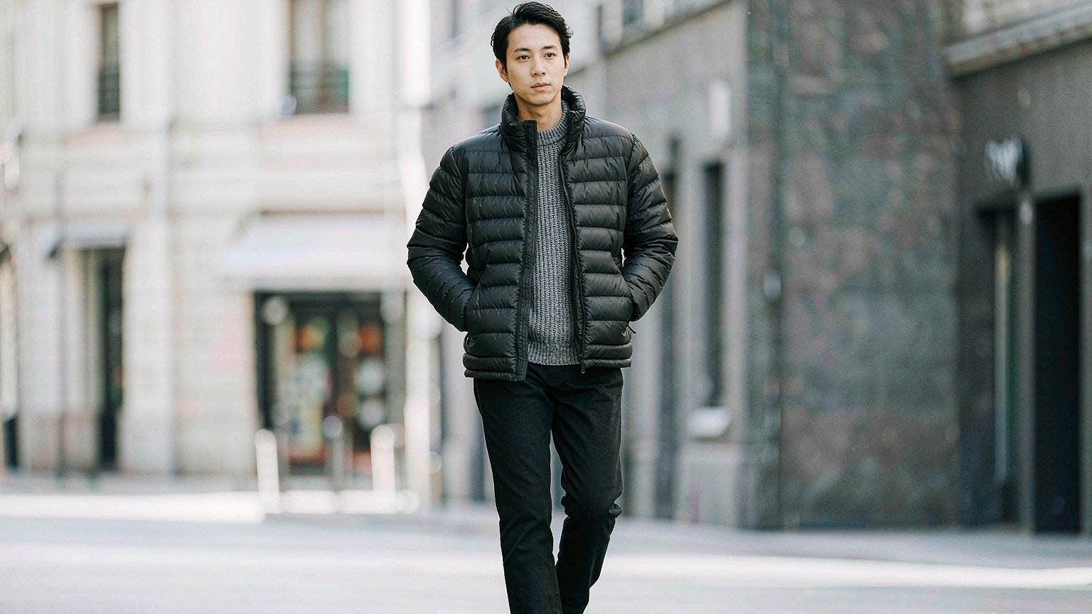 Model in a black quilted Prada-style puffer jacket on a grey city street in cold winter daylight