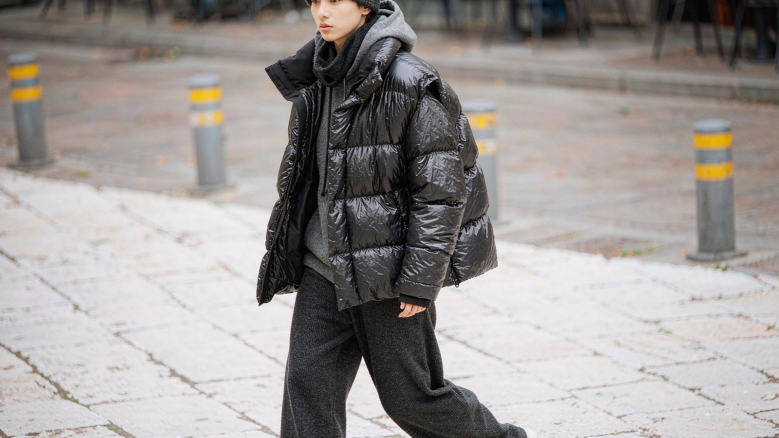 A person wearing a black glossy down vest layered over a grey hoodie on a cold city street.